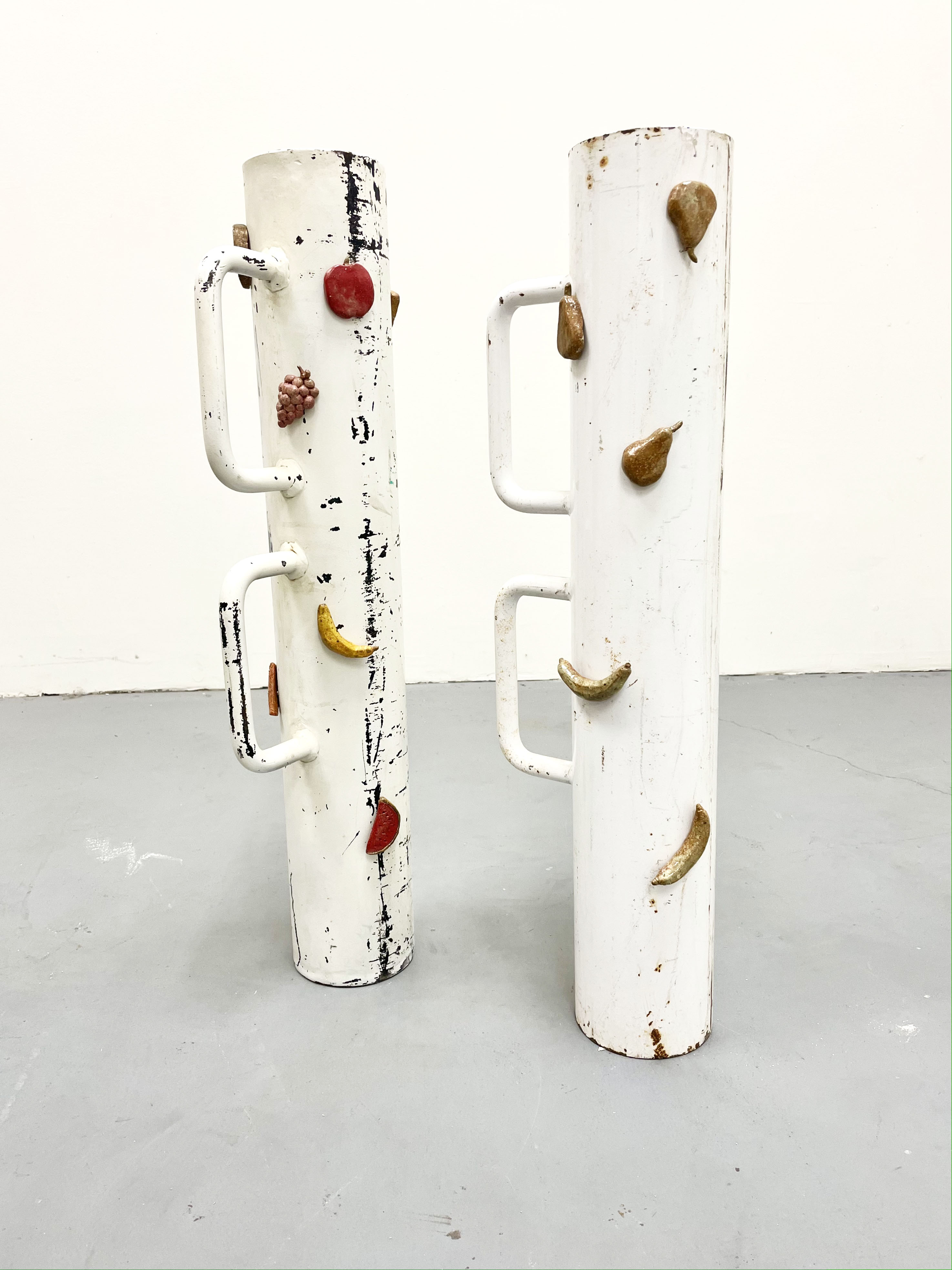A Fruited Plane - A sculpture by Brian Dario, Featuring two paint chipped battering rams standing upright with ceramic fruit magnets attatched to them