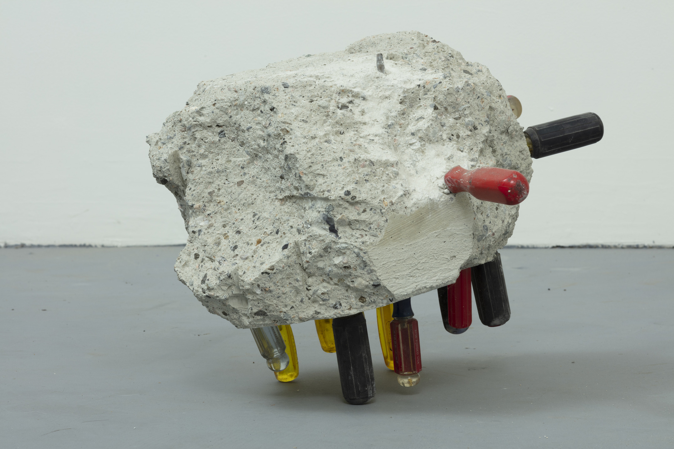 Eh Tu - A sculpture by Brian Dario, A large chunk of concrete, pierced at multiple angles by different screwdrivers, held up by the screwdrivers piercing it from the bottom