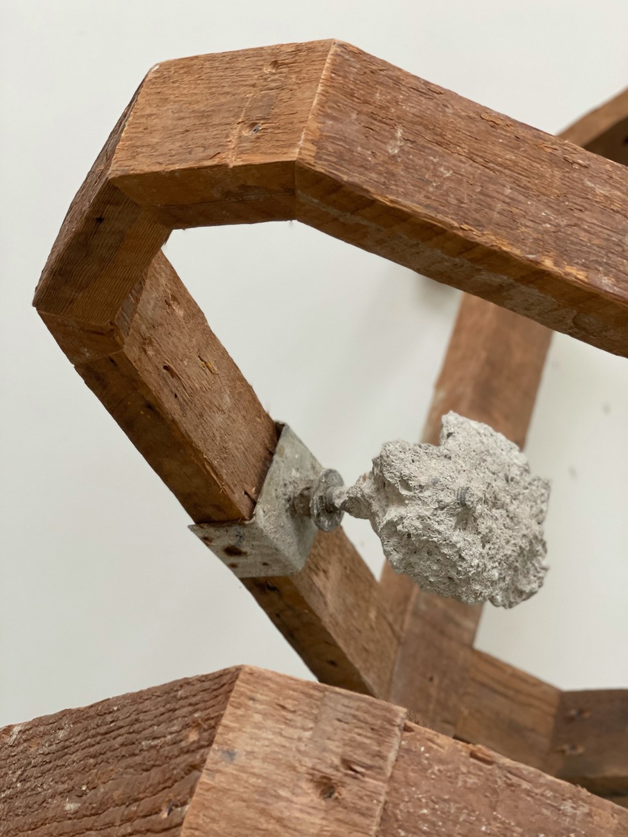 Untitled - A sculpture by Brian Dario, Closeup of a thin concrete footing chunk, attatched by screw and metal fastener to the lumber, facing in towards the volume of the sculpture